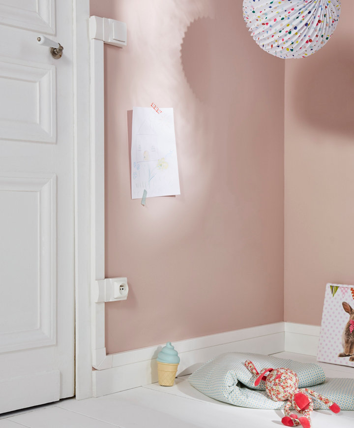 coin de pièce avec un mur rose, une prise électrique sécurisée par un cache, des objets pour enfant
