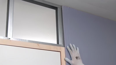 Personne qui montre une plaque de platre sur le haut d'un mur