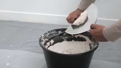 Personne qui mélange une pate de mortier dans un seau avec des spatule