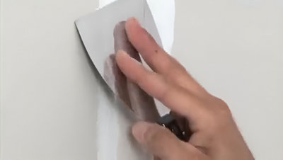 Personne qui applique l'enduit de remplissage au mur avec un spatule