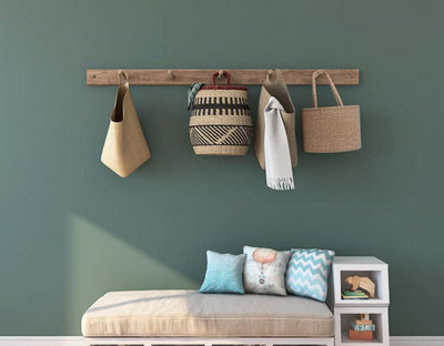 Porte manteau en bois sur mur vert et pouf en dessous