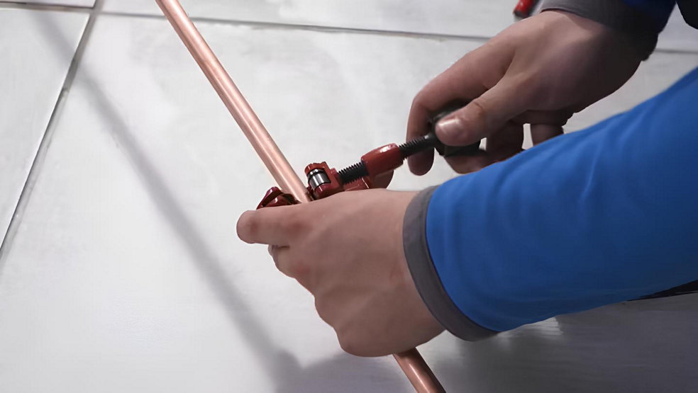 Des mains utilise un coupe tube sur un tuyau de cuivre