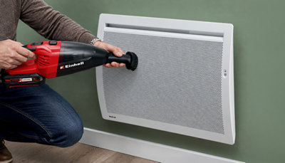 Dépoussiérage à l'aspirateur d'un radiateur électrique Noirot posé sur un mur vert