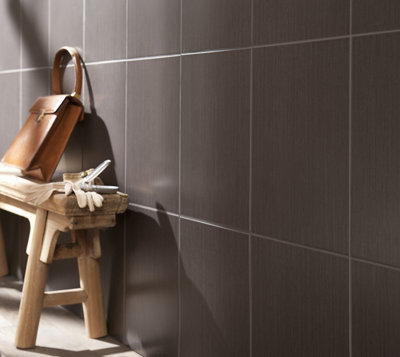 Banc en bois contre un mur carrelé sombre, avec un sac en cuir et des gants posés dessus.