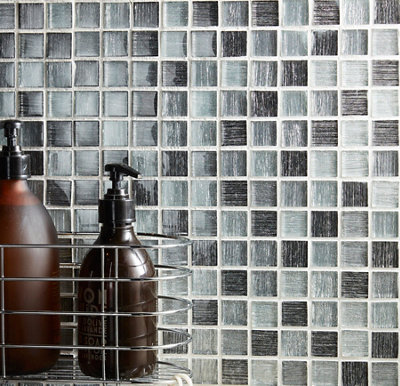 Mur en mosaïque noire et grise avec porte-savon métallique et flacons de soin.