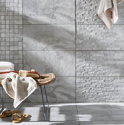 Salle de bain carrelage gris texturé, banc en rotin et accessoires en fibres naturelles.