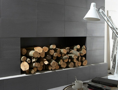 mur en carrelage gris foncé et niche intégrée pour le rangement de bûches.
