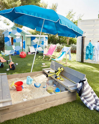Bac à sable dans jardin avec parasol et jouets
