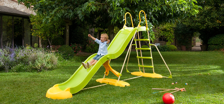 Enfant descendant un toboggan vert dans le jardin