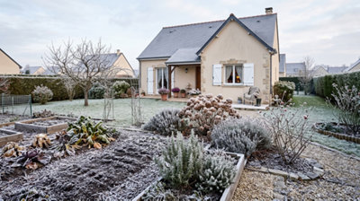 Potager en carrés et massifs de fleurs recouverts de gelée blanche devant une maison, jardin en novembre.