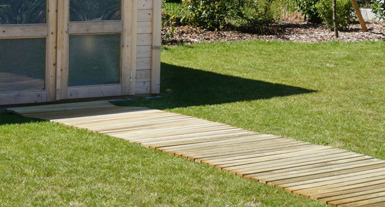 Une allée en bois menant vers un abri de jardin et traversant une pelouse