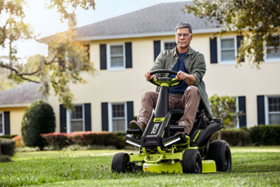 Un homme sur un rider qui tond le gazon de son jardin