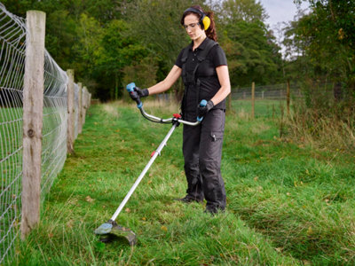 Une femme utilise une débroussailleuse le long d'une clôture