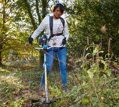 Une femme avec tous les équipements de protections individuelles travaille avec une débroussailleuse dans un sous-bois
