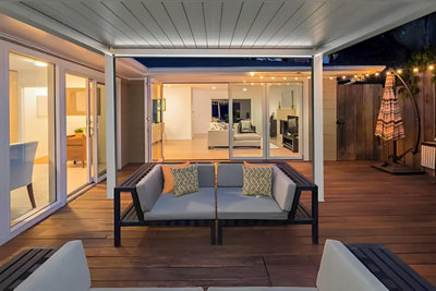 Un soir en été sous une pergola bioclimatique blanche et dans un salon de jardin confortable