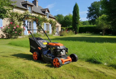 Une pelouse devant une maison individuelle à moitié tondue avec une tondeuse au premier plan