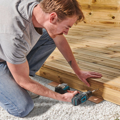 Un homme visse une planche de finition sur une terrasse