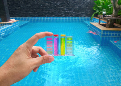 Une main présente des bandelettes de mesure de la qualité de l'eau devant une piscine