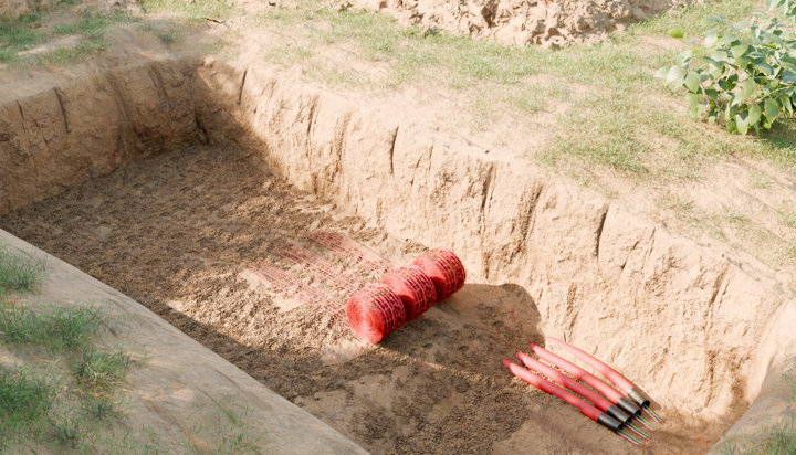 Bobines de grillages avertisseur rouge dans un trou creusé dans jardin
