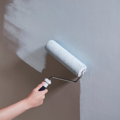 Une main passe un rouleau à peinture sur un mur