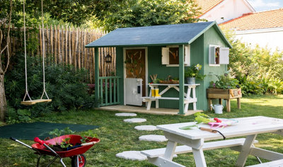 Un jardin avec un abri de jardin en bois peint, une balançoire et une table de jardin en bois peinte