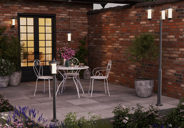 Une terrasse la nuit éclairée par un lampadaire, des potelets et des appliques