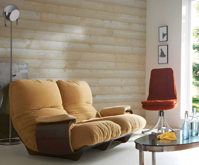 Salon avec canapé avec gros coussins jaune et chaise rouge devant mur lambris bois clair