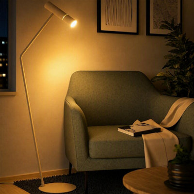 Un coin lecture chaleureux et moderne avec un fauteuil confortable éclairé par un lampadaire design aux tons chauds. Créez votre cocon.