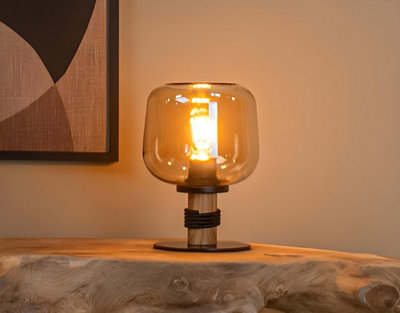 Lampe à poser design en verre ambré et pied en bois, diffusant une lumière chaleureuse dans un intérieur moderne et cosy.