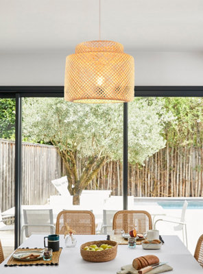 Luminaire en bambou au dessus d'une table de salon avec baie vitrée sur jardin.