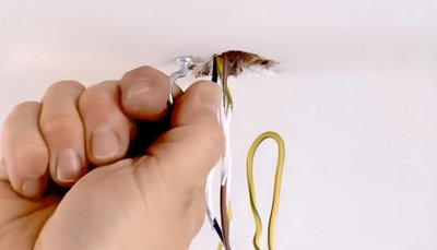 personne qui fixe crochet métallique à un plafond percé avec plusieurs fils électriques.