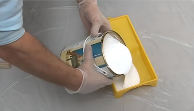 Personne qui verse de la peinture blanche dans un bac à peinture