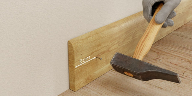 Personne avec marteau et plinthes bois avec un clou à 5cm du bord