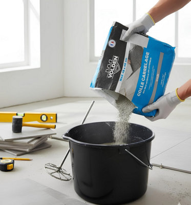 Un homme prépare un seau de colle pour démarrer son chantier de pose de carrelage