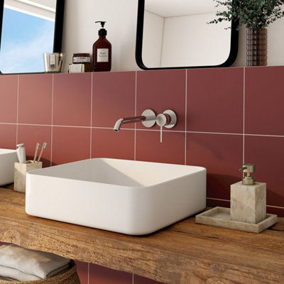 Salle de bain avec vasque carrée, carrelage rouge, plan en bois et robinet mural.
