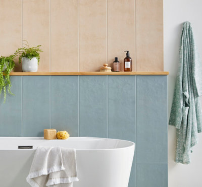 Salle de bain avec baignoire blanche, carrelage bicolore bleu et beige, et étagère bois.