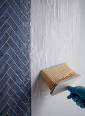 Pinceau appliquant colle sur mur avec carrelage bleu
