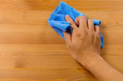 Une main passe un coup de chiffon microfibre sur un meuble en bois