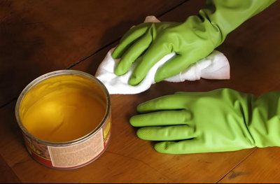 Des mains gantées passent de la cire sur un meuble en bois